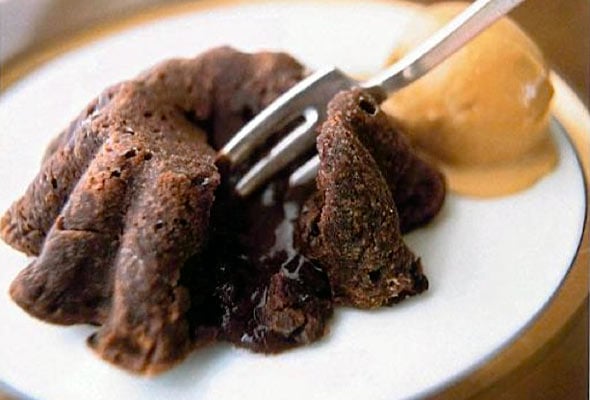 A fork cutting into a molten chocolate cake on a white plate with a scoop of ice cream.