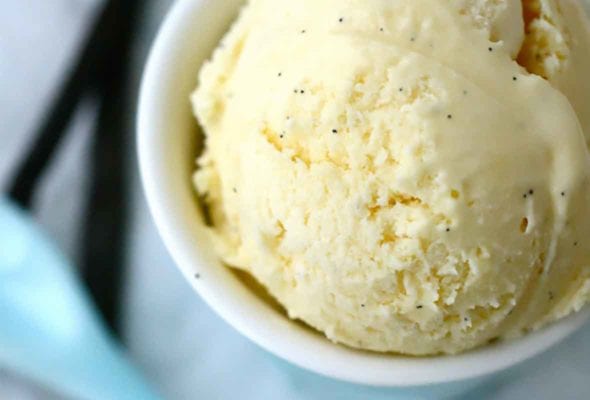 A white bowl filled with French vanilla ice cream with a blue spoon resting beside.