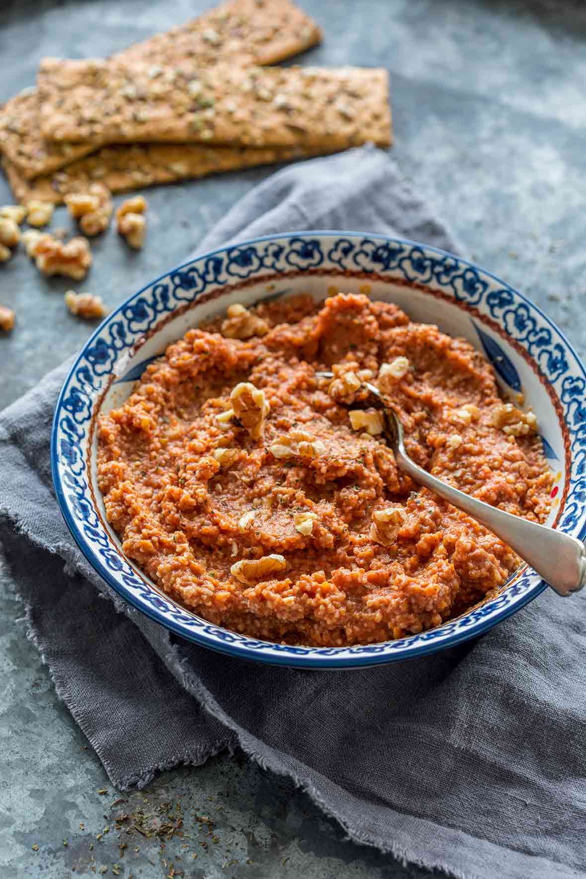 Blue and white bowl filled with Muhammara, or red pepper walnut spread with a spoon in it