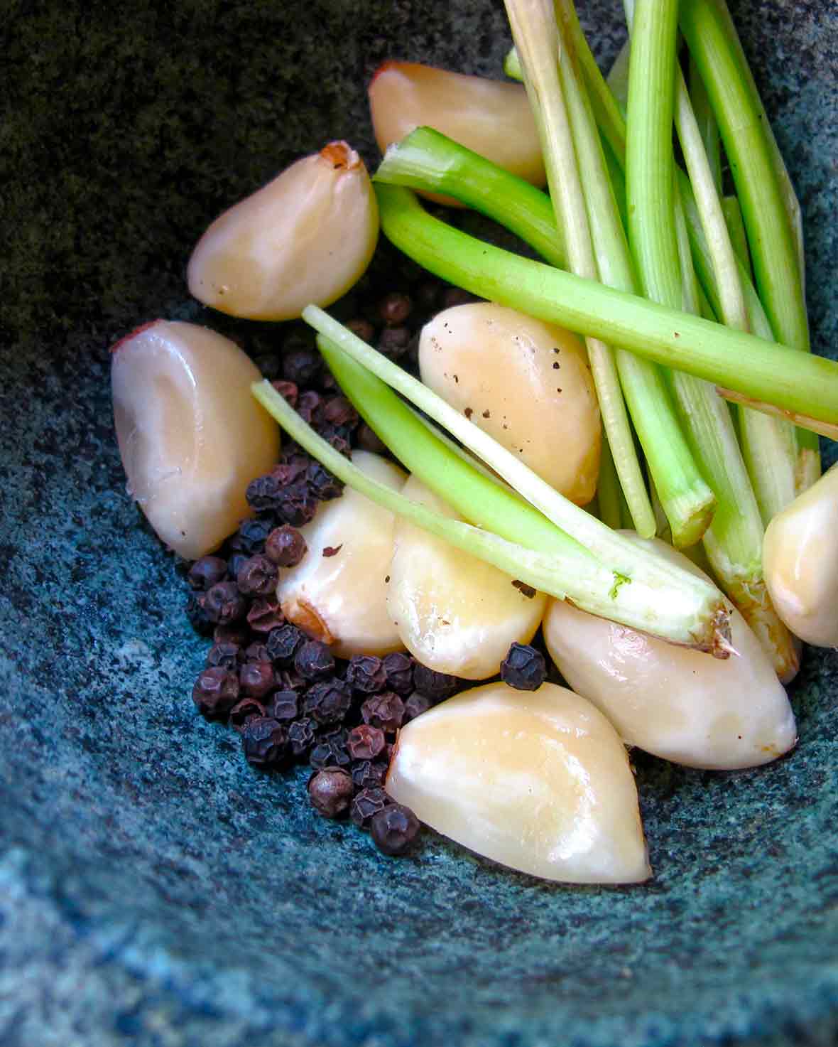 A mortar filled with ingredients for a Thai peppercorn-cilantro root paste--garlic, black peppercorns, cilantro stems