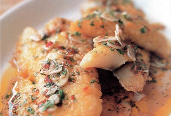 Plate of fried salt cod in a garlic-pepper sauce, on top are pepper flakes and sliced garlic cloves