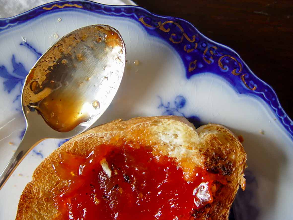 A slice of toast schmeared with Portuguese tomato jam on a decorative plate with a spoon resting beside it.