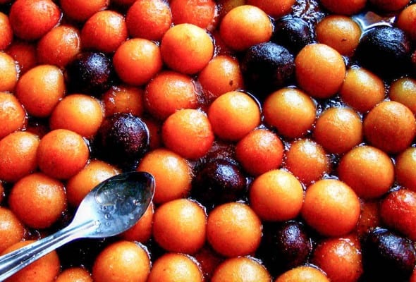 Indian milk fritters in syrup with a spoon resting on top.