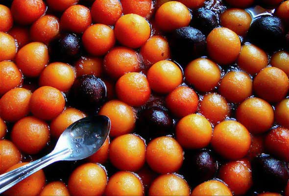 Indian milk fritters in syrup with a spoon resting on top.