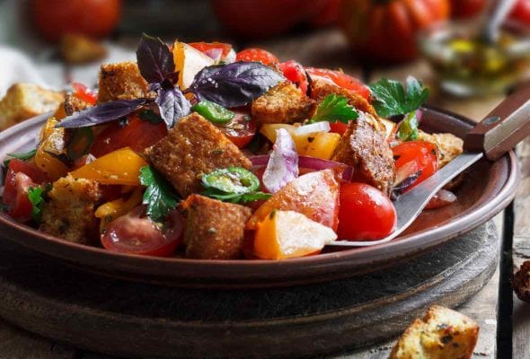Wood bowl of Barefoot Contessa panzanella with bread chunks, tomatoes, peppers, cucumbers, basil, and parsley