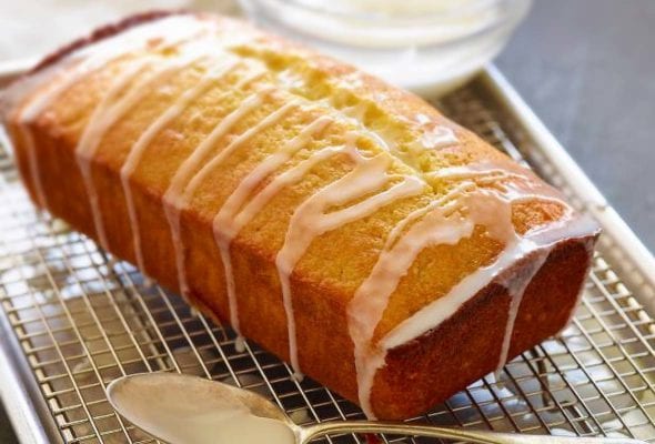 Ina Garten's lemon cake, a pound cake, on a rack, drizzled with a lemon glaze, a spoon nearby