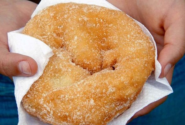A child holding a malassadas, or Portuguese doughnut, in a paper napkin.