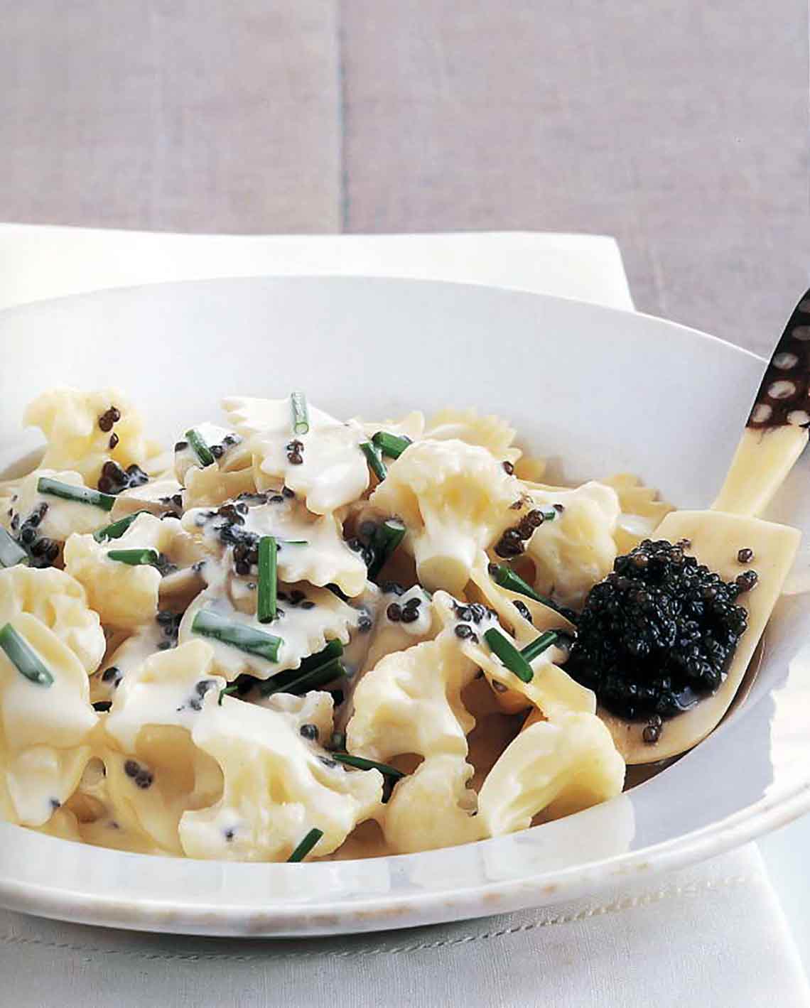 A bowl of bowtie pasta with caviar, in a cream sauce topped with chives