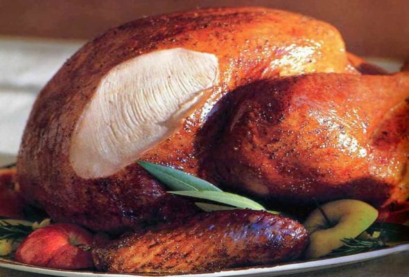 A classic roast turkey on a platter with pieces of apple and rosemary sprigs tucked around it.