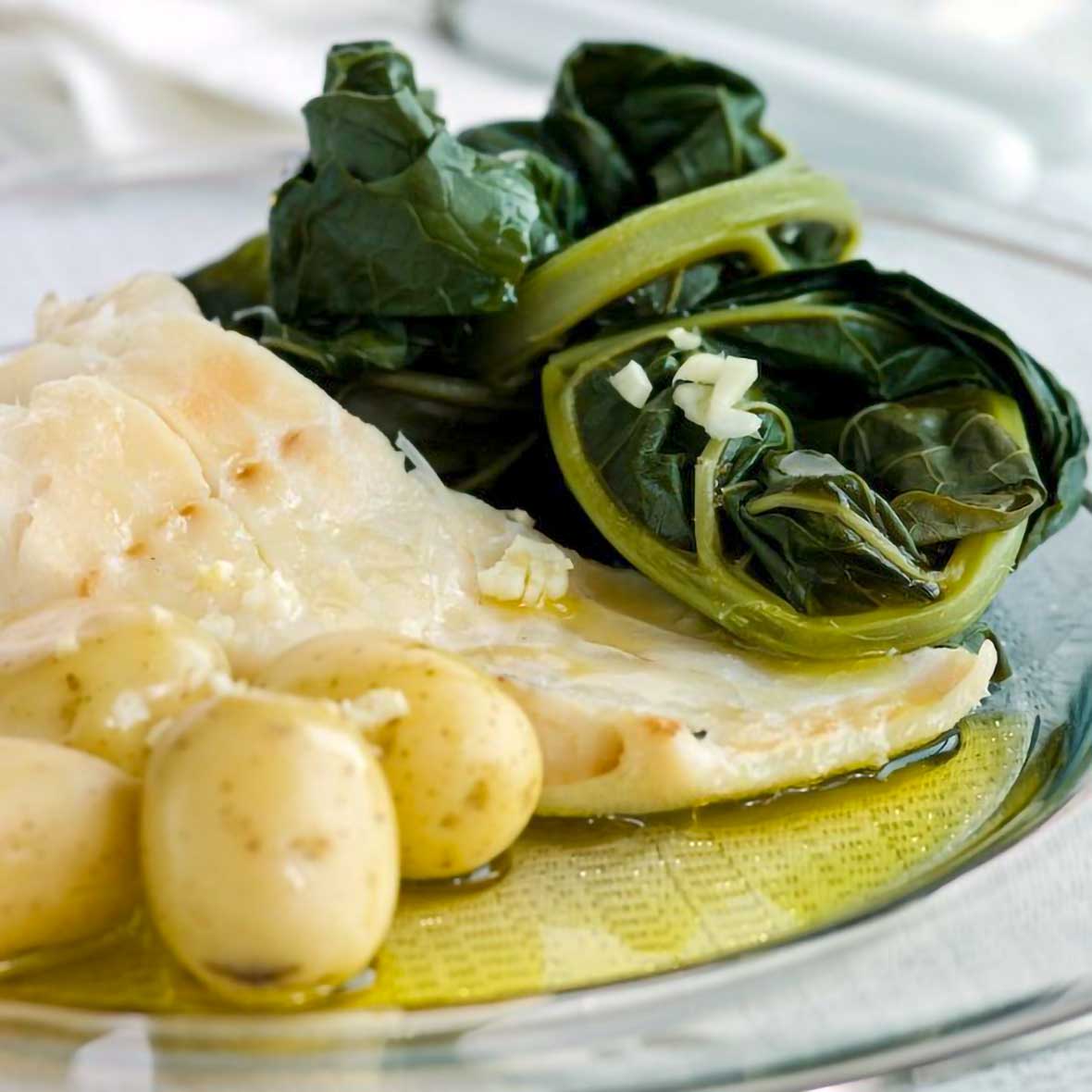 A white plate of bacalhau consoada or Portuguese Christmas Eve cod, with salt cod, small potatoes, and blanched kale