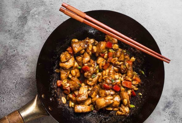 A wok filled with kung pao chicken with two chopsticks on the edge