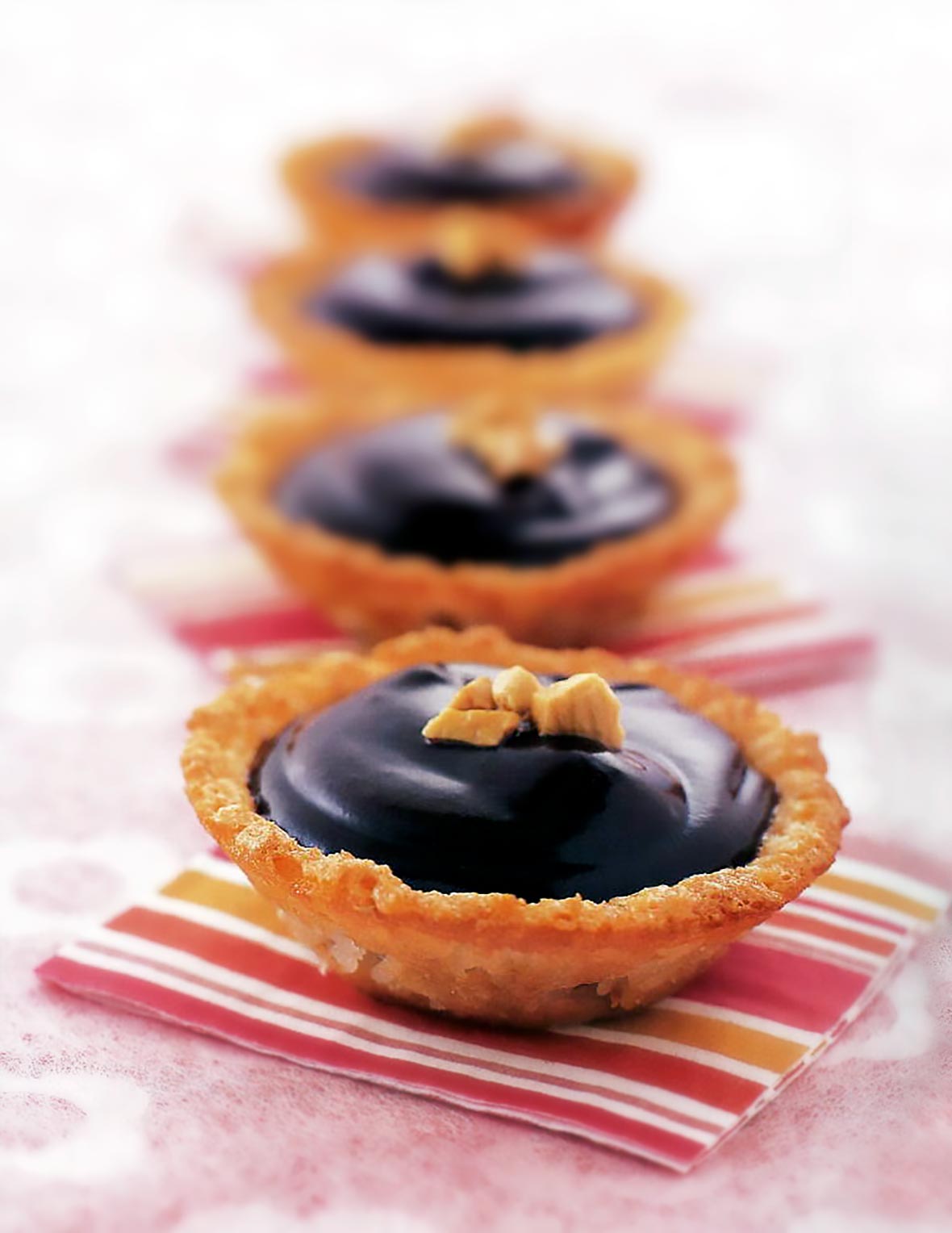 Four chocolate coconut macaroon pies, each resting on a striped cocktail napkin.