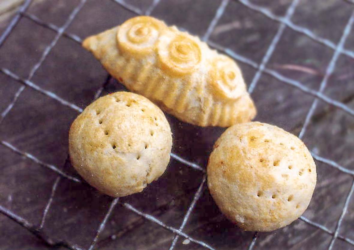 Three cookies--two balls, one oblong--with circular and perforations decorations on top on a wire rack