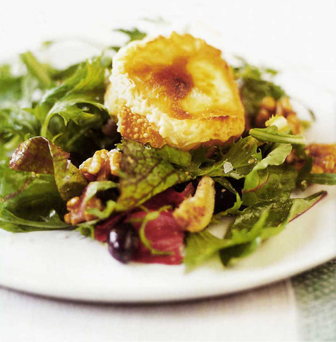 Mixed green salad with a slice of baguette and got cheese on top