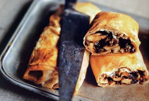 Two mushroom strudels on a silver tray, one cut in half, with a knife resting on top.