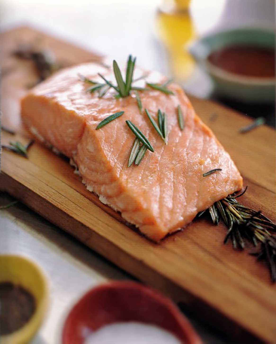 Filet of salmon topped with rosemary leaves on a cedar plank