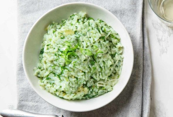 A white bowl filled with spinach and arugula risotto on a grey linen napkin.