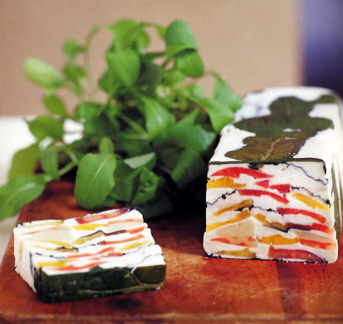 A loaf of tomato-goat cheese terrine--garlicky goat cheese layered with red and yellow tomatoes and arugula on a cutting board
