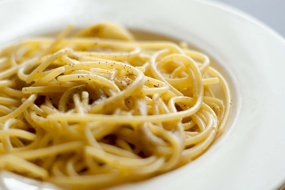 A tangle of cacio e pepe noodles in a white bowl.
