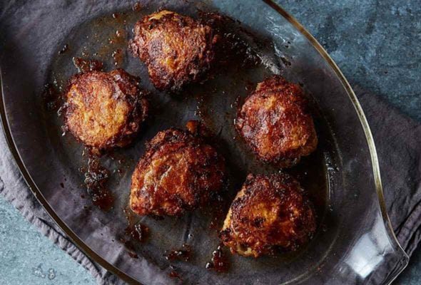 A casserole dish with five chicken thighs that have been oven-fried set on top a dish towel