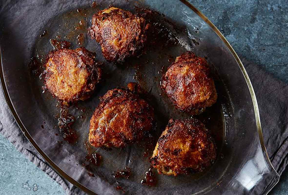 A casserole dish with five chicken thighs that have been oven-fried set on top a dish towel