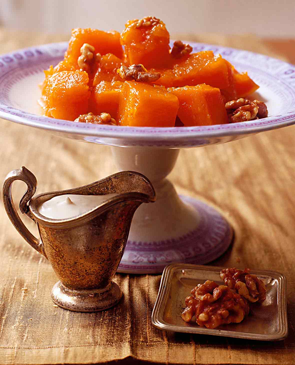 A decorative stand with a pile of cubed cooked pumpkin that is topped with walnuts.