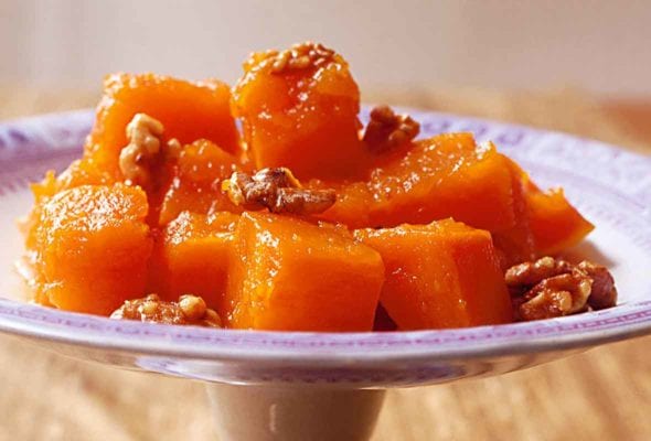 A decorative stand with a pile of cubed cooked pumpkin that is topped with walnuts.