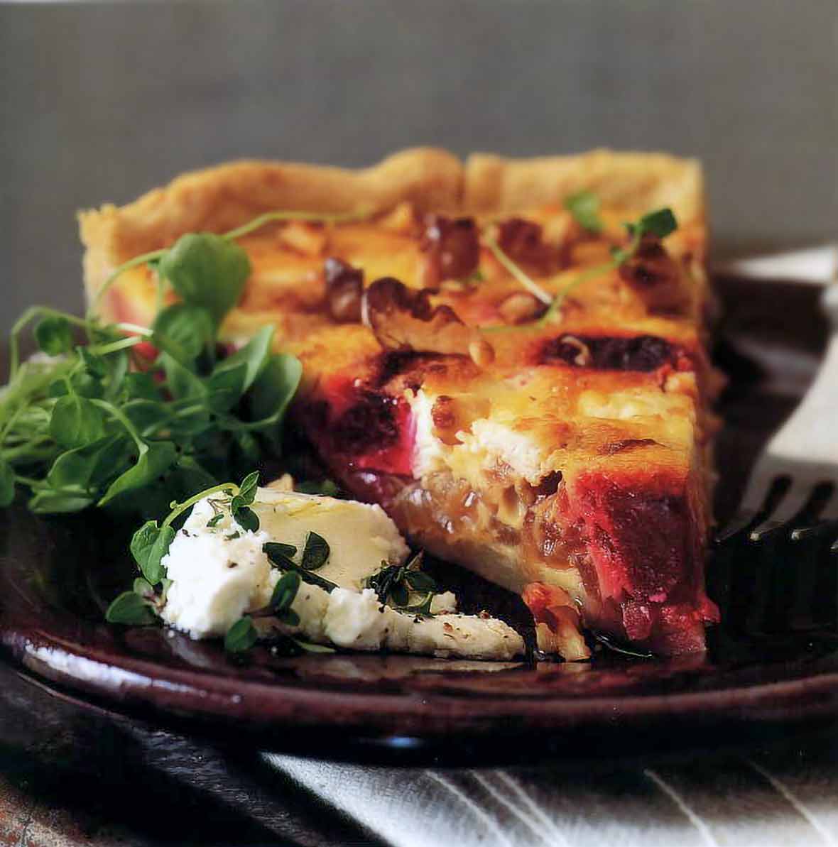 A slice of goat cheese, roasted beet, and walnut tart, goat cheese and watercress on the side