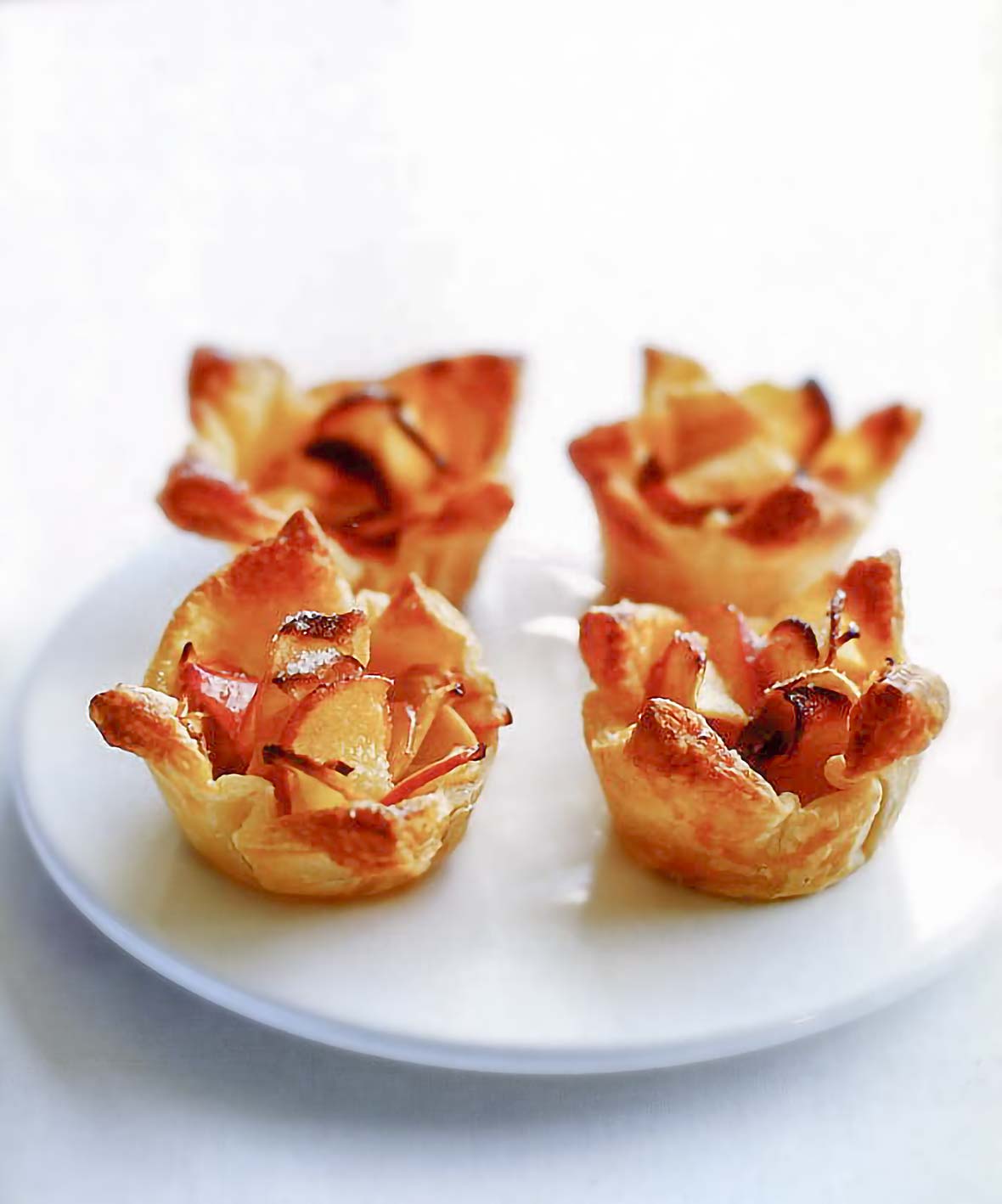 Four mini apple tarts made from apple slices in puff pastry shells on a plate