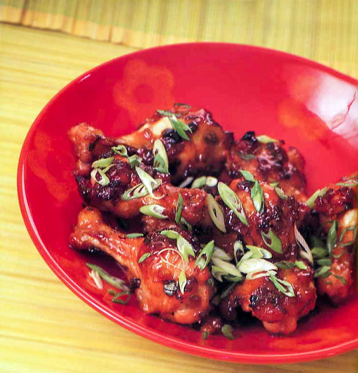 A red bowl filled with mahogany wings that are sprinkled with sliced scallions.