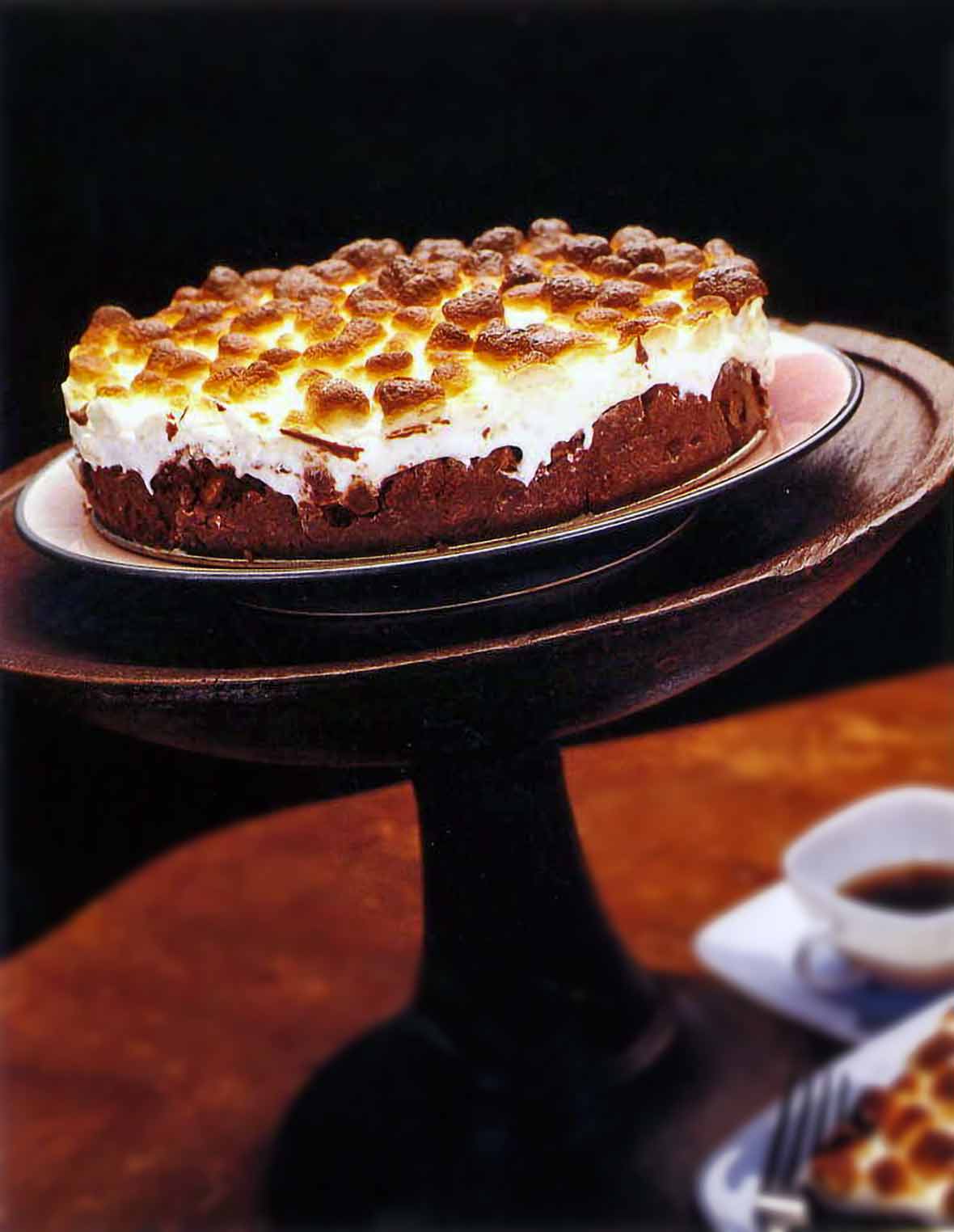 Mississippi mud cake topped with toasted marshmallow in a wooden cake stand
