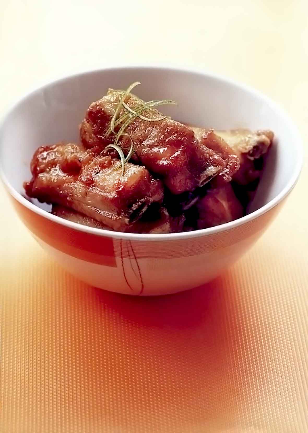 A bowl with three spare ribs glossed with a sweet-sour sauce, on top lime zest