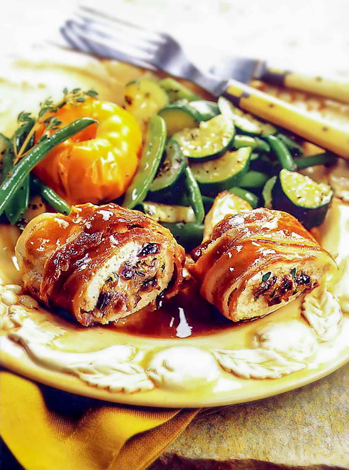 A plate with two chicken breasts wrapped in goat cheese and proscuitto along side vegetables