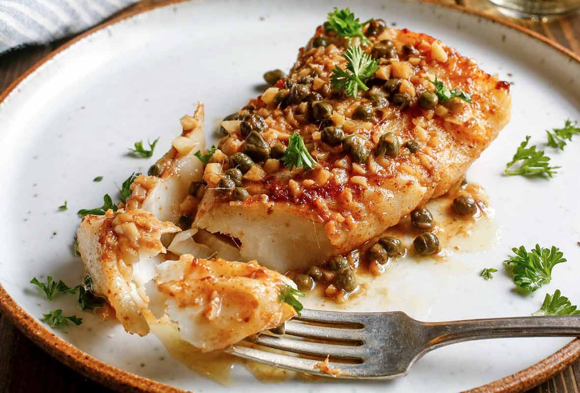 Pan-roasted halibut with caper vinaigrette on a white plate sprinkled with parsley