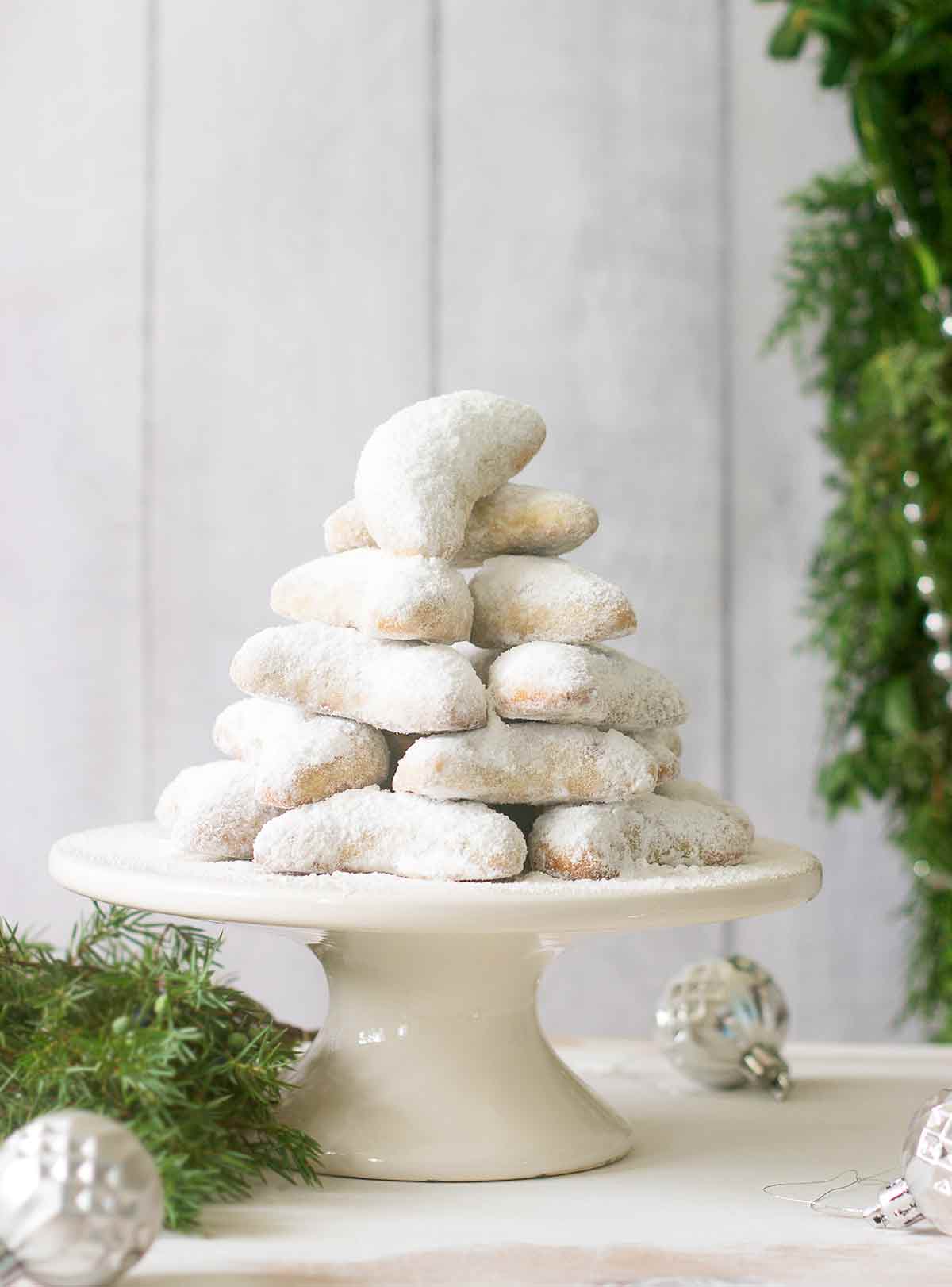 A stack of walnut crescents on a white stand with Christmas decorations and greenery around them.