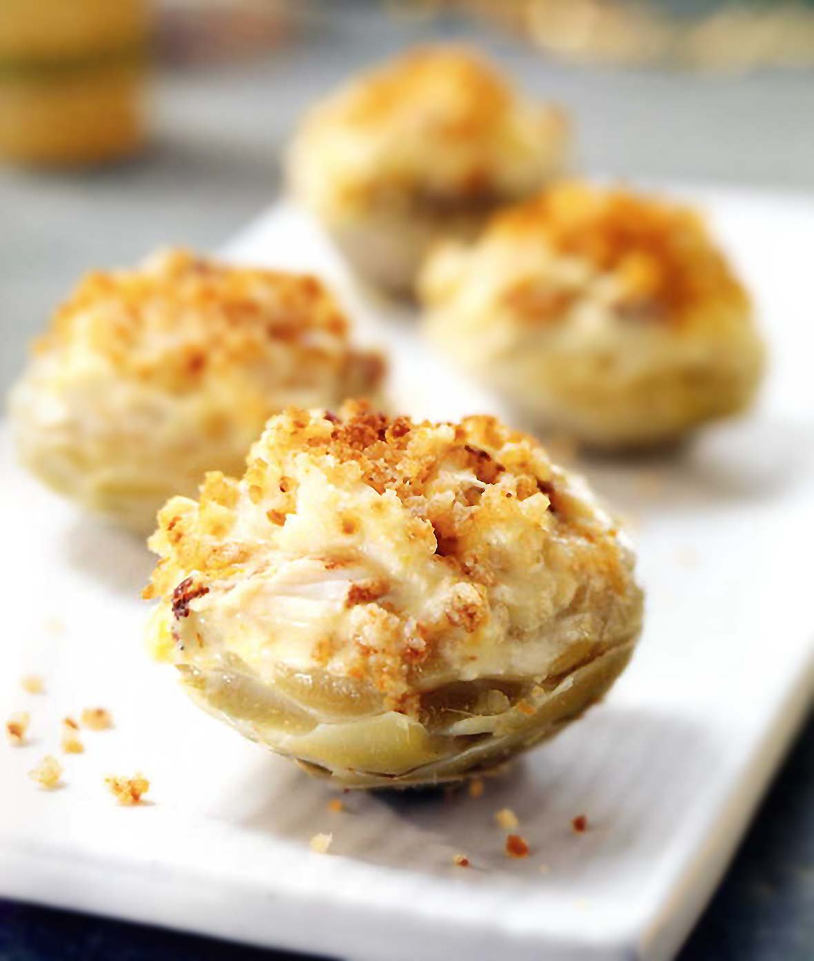 Four artichoke hearts stuff with saffron-scented crab, topped with toasted bread crumbs, on a white plate