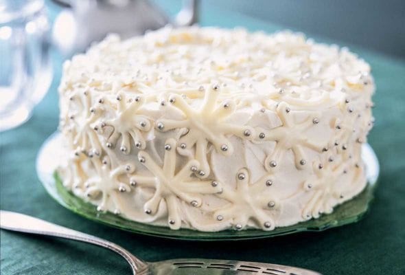 A snowflake cake decorated with white chocolate snowflakes and silver dragees on a green plate.