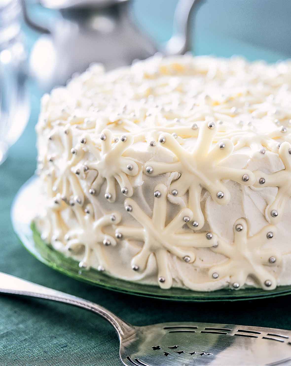 A snowflake cake decorated with white chocolate snowflakes and silver dragees on a green plate.