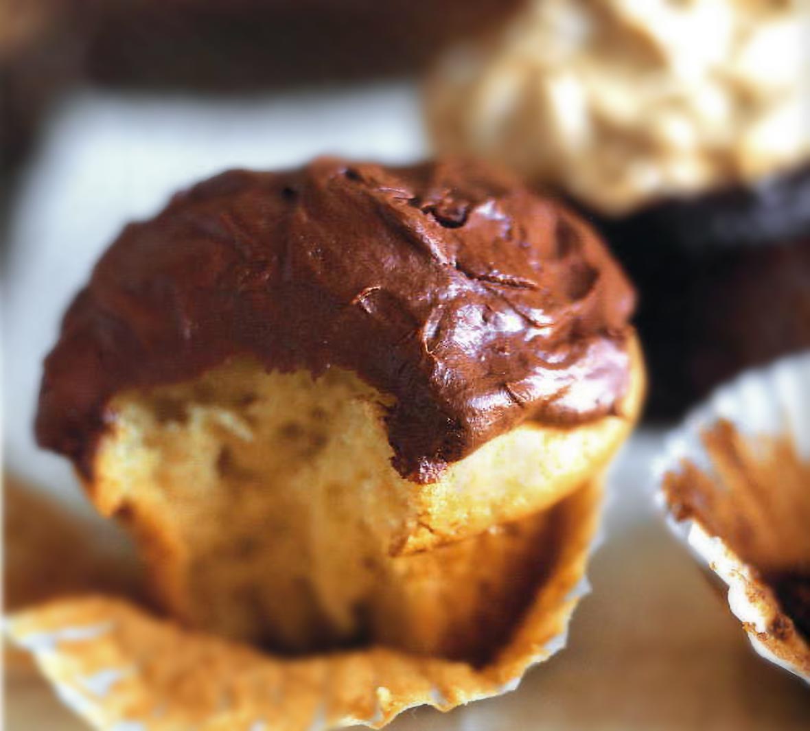 A white cupcakes with chocolate frosting in its paper wrapper and a bite taken out of it