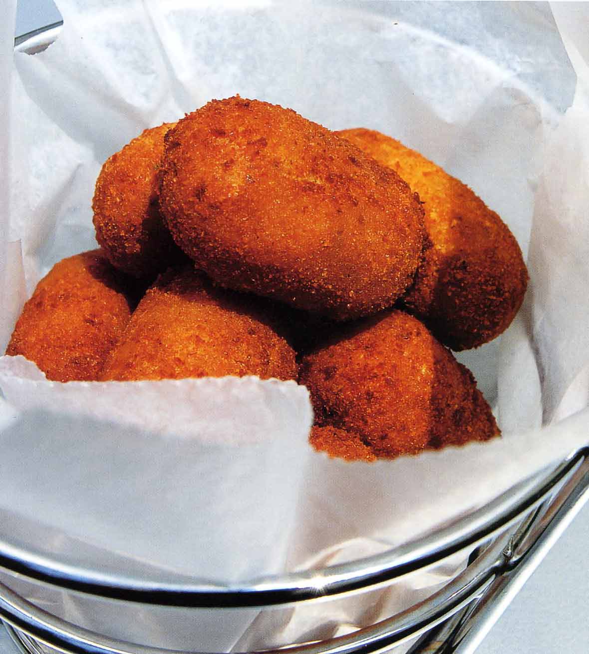 Batch of deep-fried oval Spanish serrano ham and chicken fritters in a metal basket