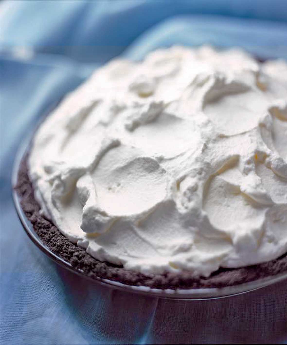 A chocolate cream pie, with a chocolate crumb crust and topped with whipped cream, on a blue background