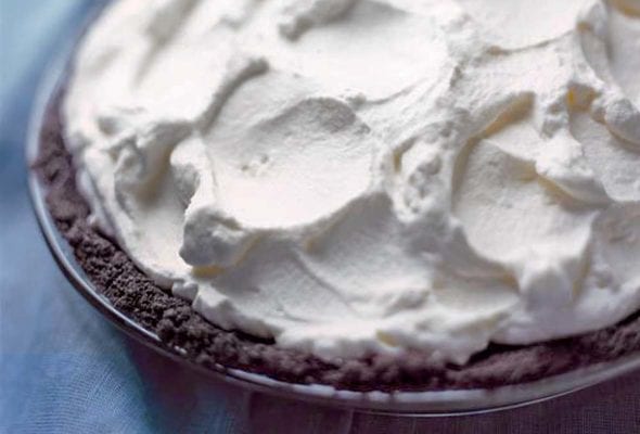 A chocolate cream pie, with a chocolate crumb crust and topped with whipped cream, on a blue background