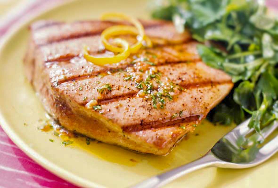 A grilled tuna steaks with spiced vinaigrette with lemon zest on top, a salad on the side