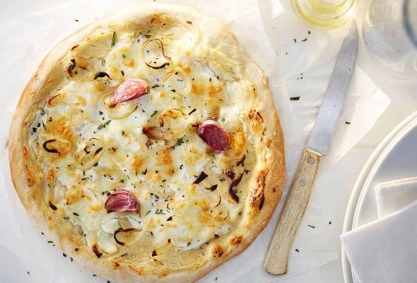 A rosemary red onion pizza with ricotta cheese, garlic cloves, and Parmesan cheese on parchment paper