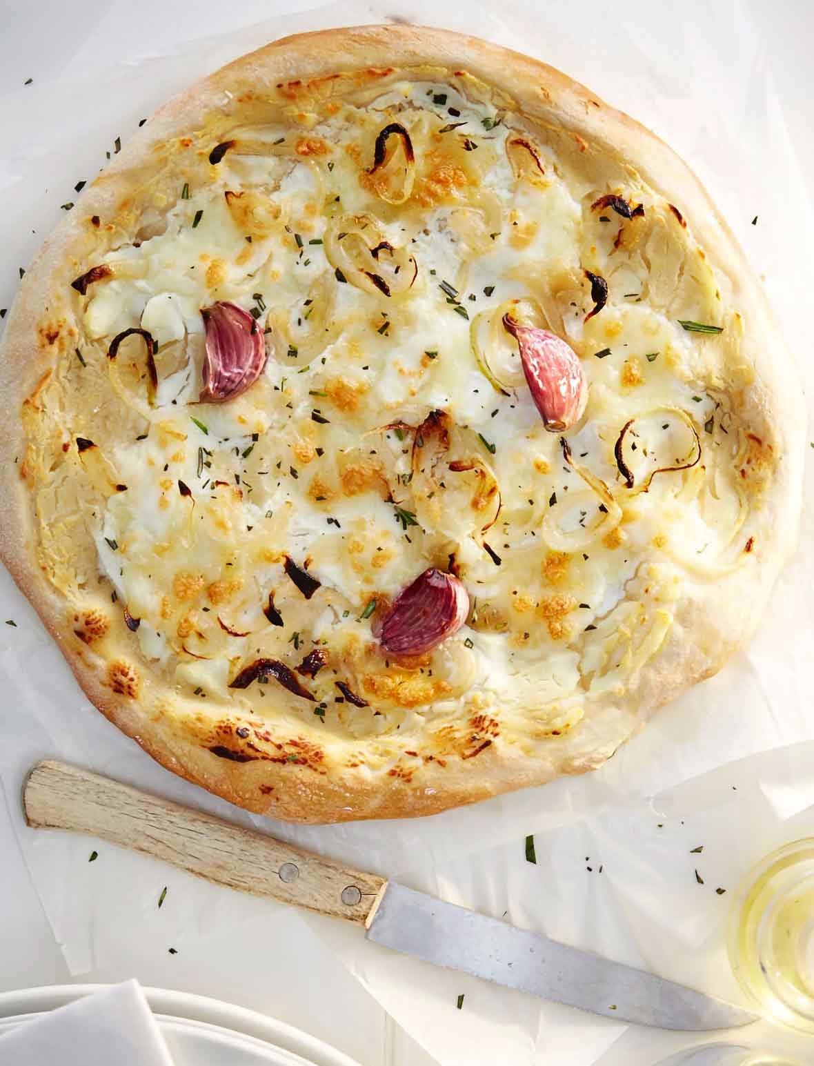 A rosemary red onion pizza with ricotta cheese, garlic cloves, and Parmesan cheese on parchment paper