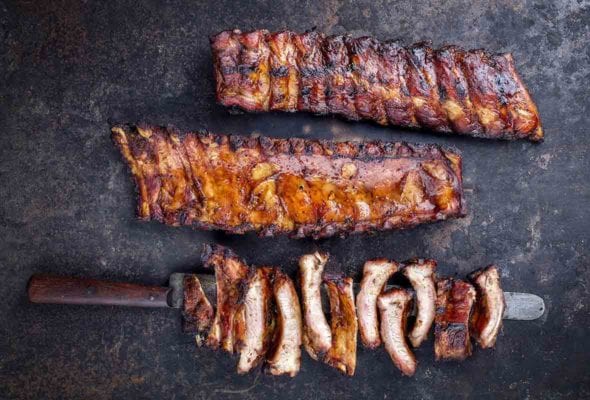 Two racks of barbecued baby back ribs, and a third rack cut into individual ribs, resting on a knife.