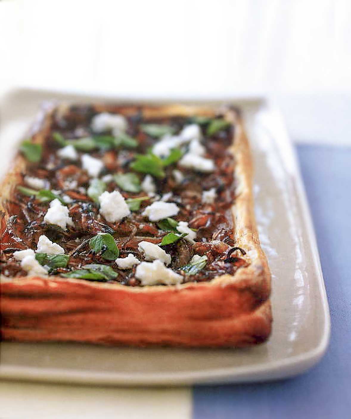 An onion and feta cheese tart with a puff pastry crust filled with caramelized onions, crumbled feta cheese, and basil