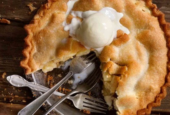 A classic apple pie with one-quarter missing, topped with a scoop of ice cream, and three forks in the empty pie spot.