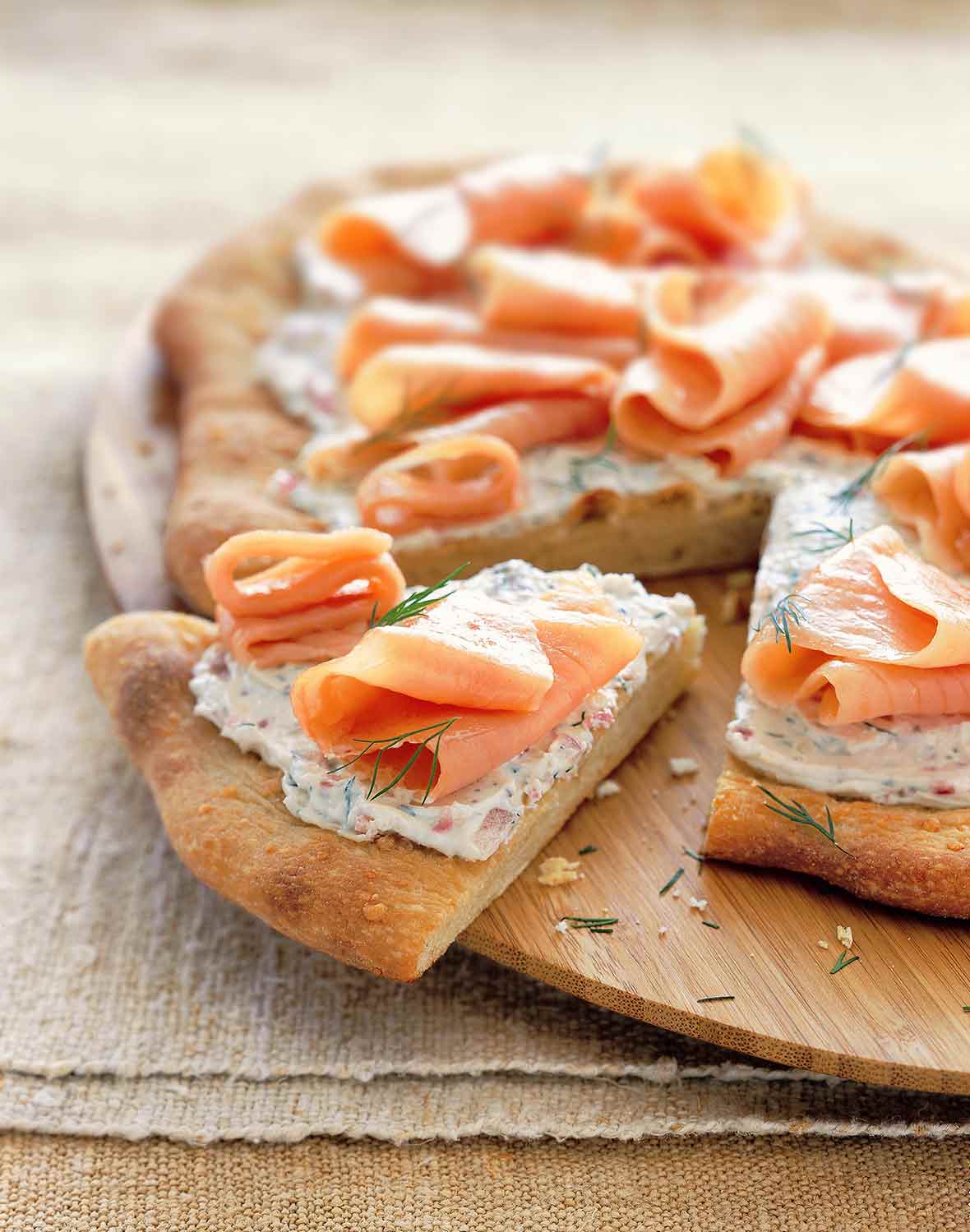 A smoked salmon pizza with cream cheese, red onion, and dill with one wedge cut out.