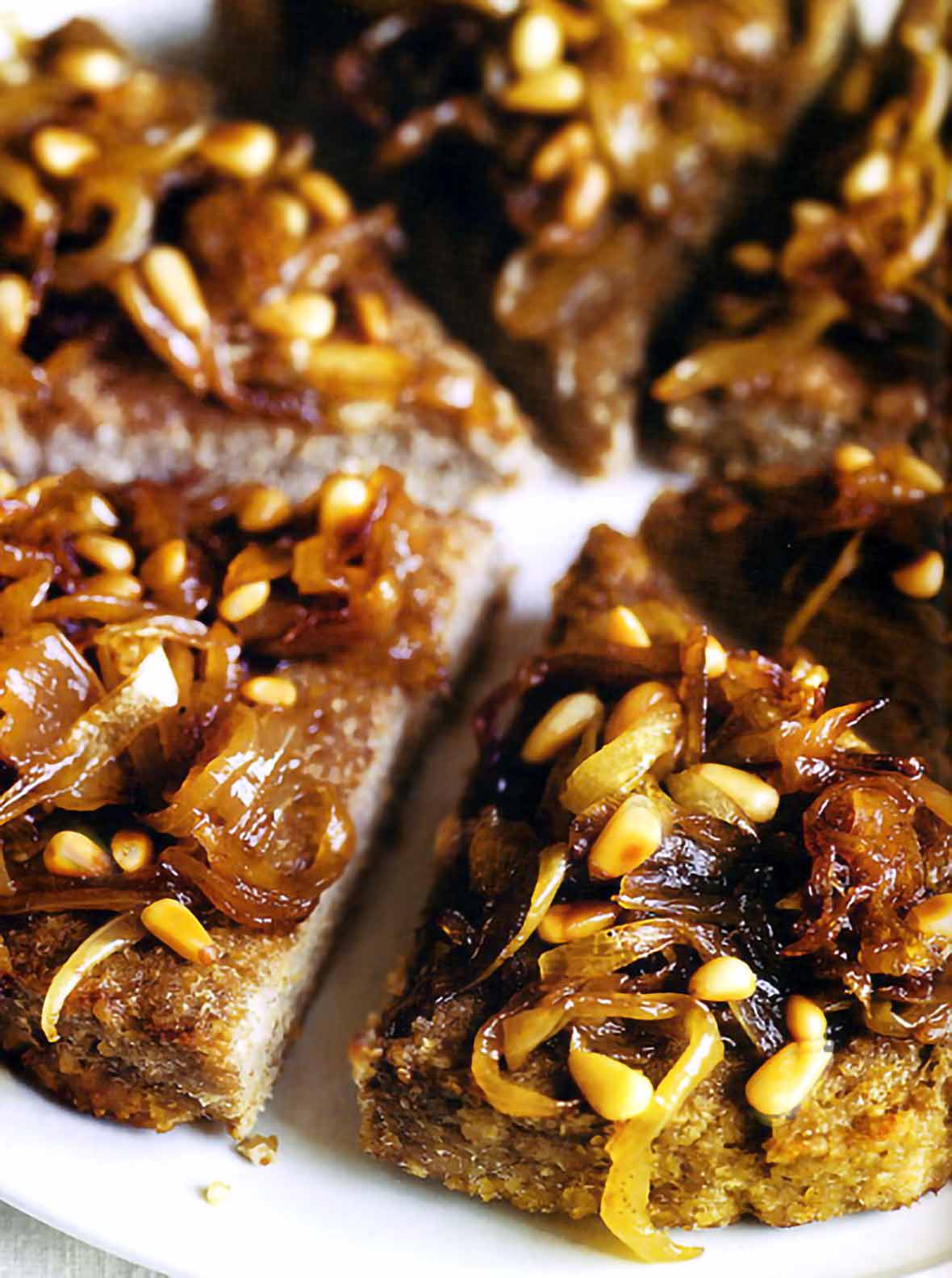 Lamb kibbeh cut into wedges topped with caramelized onions and toasted pine nuts